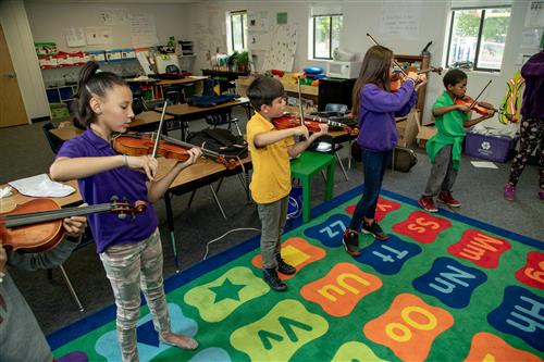 Students playing violins in a classroom 